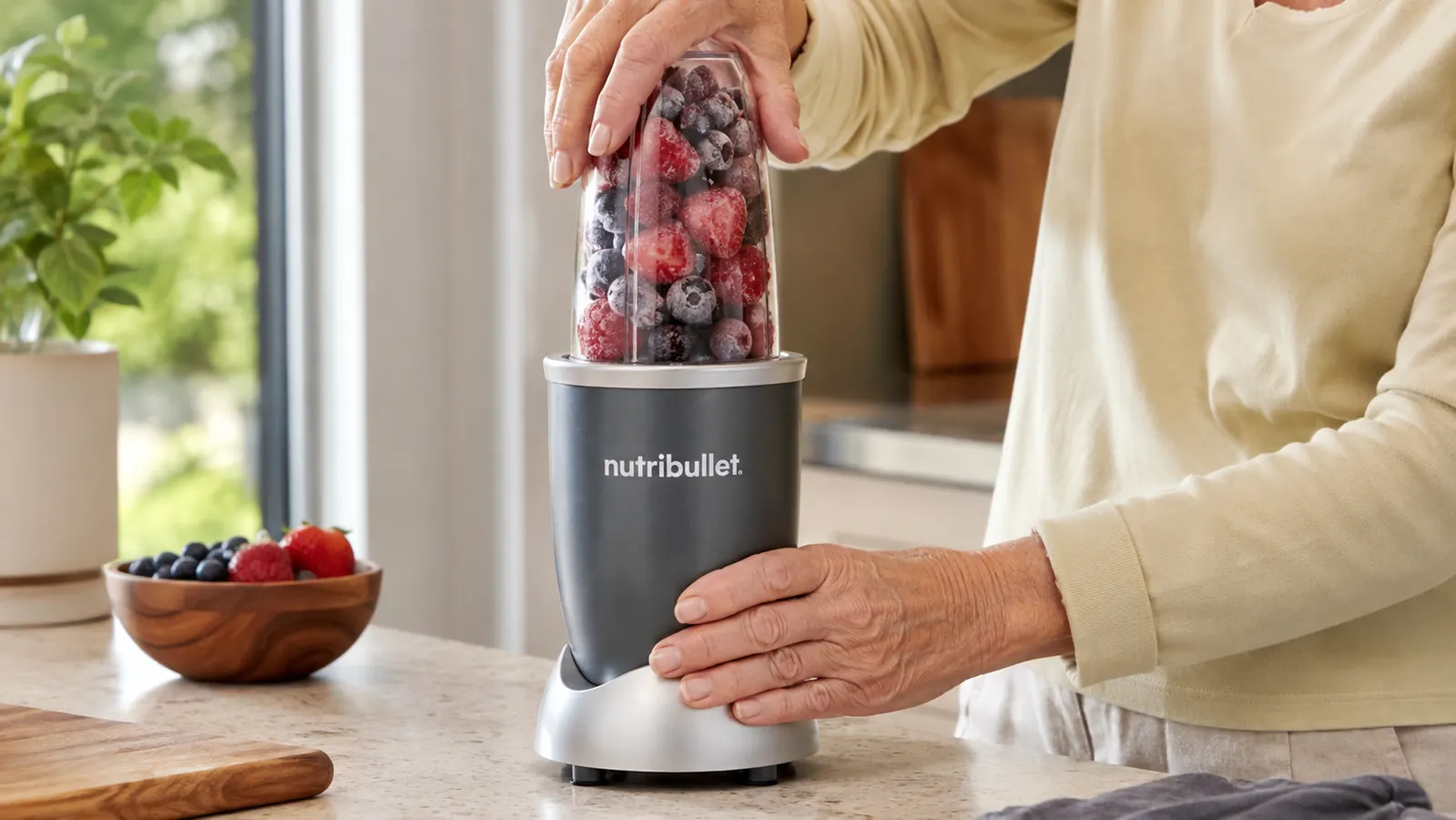 A woman's hand twisting a personal blender cup filled with frozen berries onto its base